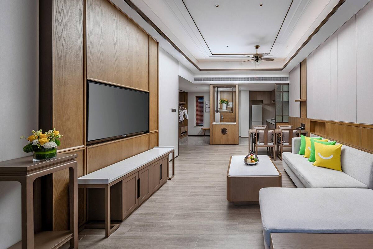 A modern living room with a flat-screen TV, wooden cabinets, a sofa with cushions, a coffee table, and a ceiling fan.
