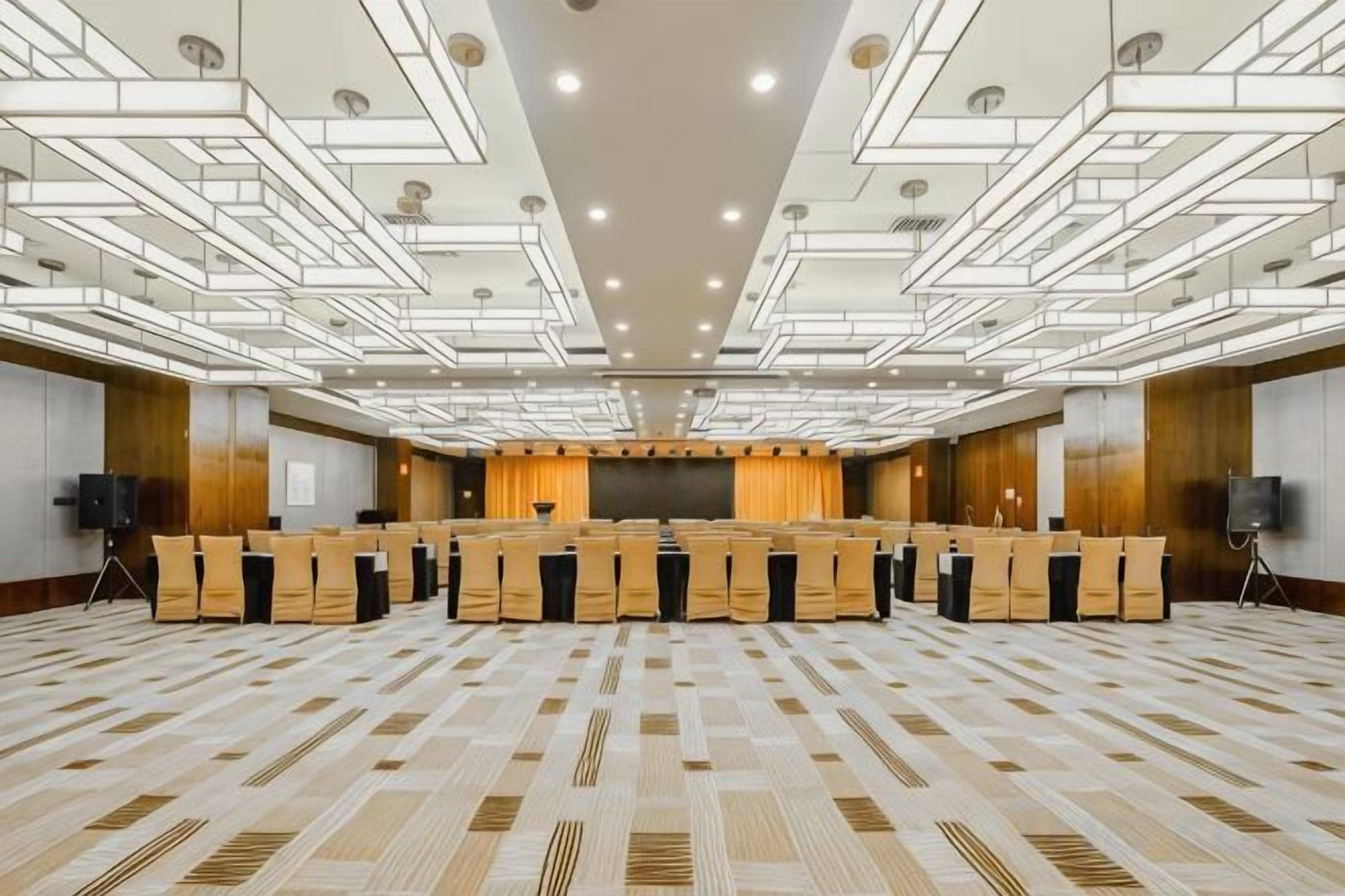 Un salón de conferencias con una larga mesa, varias sillas, una pantalla de proyector y un escenario.