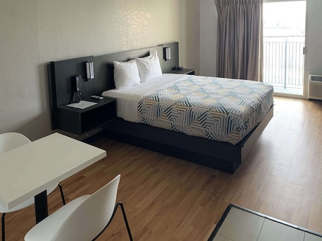 A modern hotel room with a bed, bedside tables, a desk, and chairs.