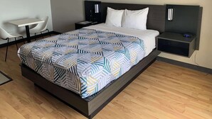 A modern hotel room with a large bed, a bedside table, a small desk with a chair, and a wall-mounted TV. - Studio 6 Lincoln, NE - Airport (Lincoln)