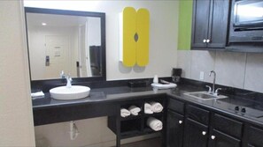 Modern bathroom with a large mirror, sink, and countertop, featuring a microwave and towel storage.