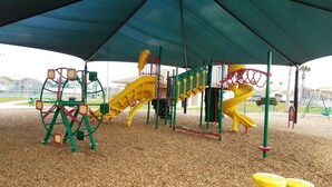 A playground with a climbing structure, a slide, and a swing set.