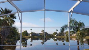 A covered outdoor area with a pool reflecting palm trees and houses.