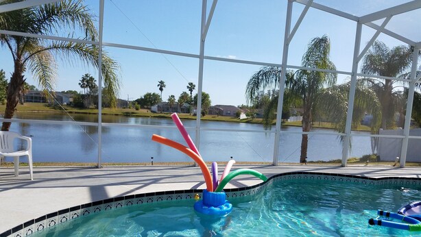 A clear swimming pool with a view of a lake and palm trees.