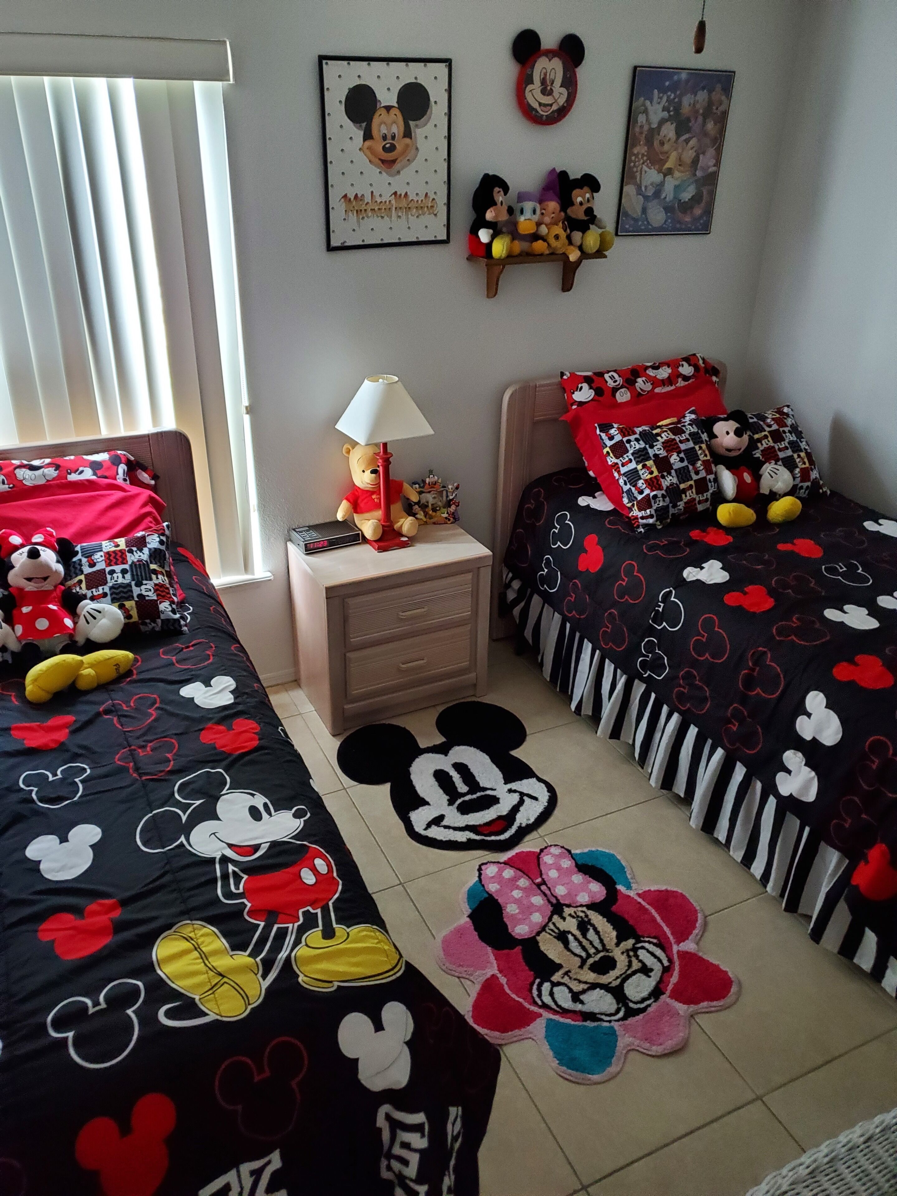 Ein Kinderzimmer mit Mickey Mouse Bettwäsche, einem Nachttisch mit Lampe sowie Wanddekorationen wie gerahmte Bilder und Stofftiere.