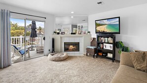 Ein Wohnzimmer mit Kamin, Fernseher und Balkon mit Gartenmöbeln.