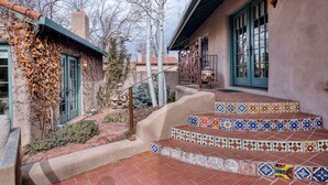 A staircase with colorful tiles leading to a building with a green door and a lantern on the wall. - Casa Dos Truchas | Adobe Retreat (Santa Fe)