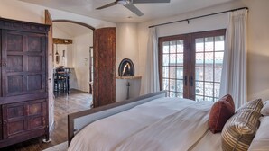A bedroom with a large bed, a wooden wardrobe, a fireplace, and a balcony with a view. - Casa Dos Truchas | Adobe Retreat (Santa Fe)