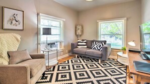 A living room with a grey sofa, a white armchair, a patterned rug, and a clock on the wall. - Historic Apartment - Walk to CSU Campus + Old Town (Fort Collins)