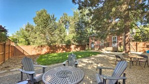 A backyard with a round table and four Adirondack chairs, surrounded by a wooden fence and trees. - Historic Apartment - Walk to CSU Campus + Old Town (Fort Collins)