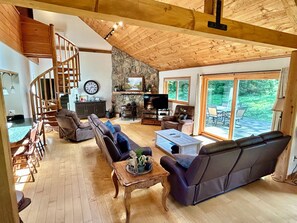 A spacious living area with a wooden ceiling, a stone wall, a fireplace, a television, and a view of the outdoors through large sliding doors.