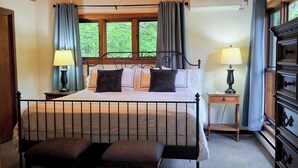 A bedroom with a sloped ceiling, a bed with a headboard, two bedside tables with lamps, a wooden dresser, and a window with curtains.