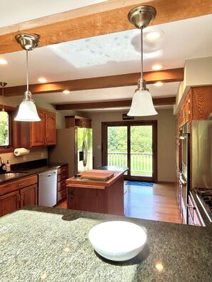 A kitchen with granite countertops, wooden cabinets, stainless steel appliances, pendant lighting, and a view to the outside.