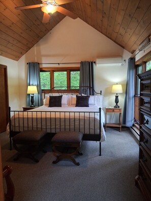 Une chambre à coucher comprenant un lit, deux tables de chevet, une fenêtre, un ventilateur de plafond et une commode.