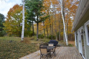 A wooden deck with outdoor furniture, surrounded by trees with autumn foliage.