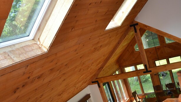 A high-ceilinged room with wooden beams, large windows, a sofa, and a dining area.