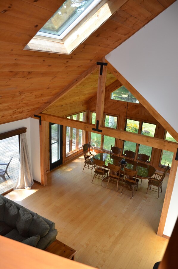 A spacious loft with a high ceiling, large windows, and a dining area with wooden furniture.