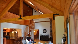 A spacious living area with a high ceiling, wooden beams, a staircase, a kitchen, and a dining area.