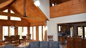 A spacious living area with a high ceiling and wooden beams, a dining area with wooden chairs, and a kitchen with wooden cabinets and a bar area.