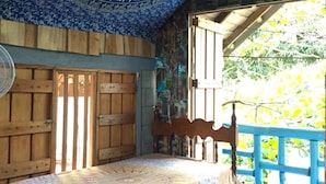 A bedroom with a bed, wooden walls, a blue ceiling with a circular design, and a view of greenery outside. - Anne's Place (La Fortuna)