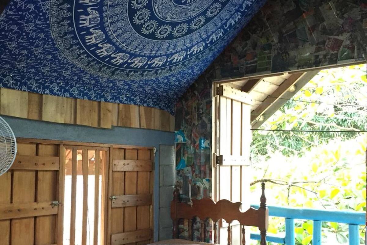 Un dormitorio con cama, paredes de madera, techo azul con diseño circular y vistas al exterior.