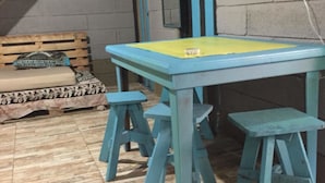 A room with a blue and yellow table, four blue stools, a wooden bench, and a fan on the wall. - Anne's Place (La Fortuna)