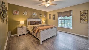 Une chambre à coucher comprenant un lit, des tables de chevet, un ventilateur de plafond, une fenêtre avec des rideaux et des éléments de décoration murale.
