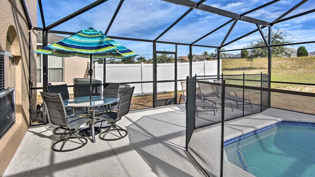 Un espace extérieur abrité comprenant une piscine, une table avec des chaises et un grand parasol.