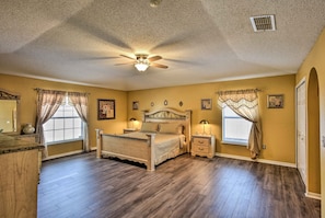 A bedroom with a wooden floor, a bed with a headboard, two bedside tables with lamps, and a ceiling fan.