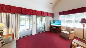 Una sala de estar con alfombra roja, televisor, sofá y comedor con mesa y sillas.