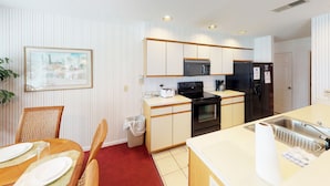 Una cocina compacta con microondas, estufa y refrigerador, un comedor con mesa y sillas, y un cuadro en la pared.