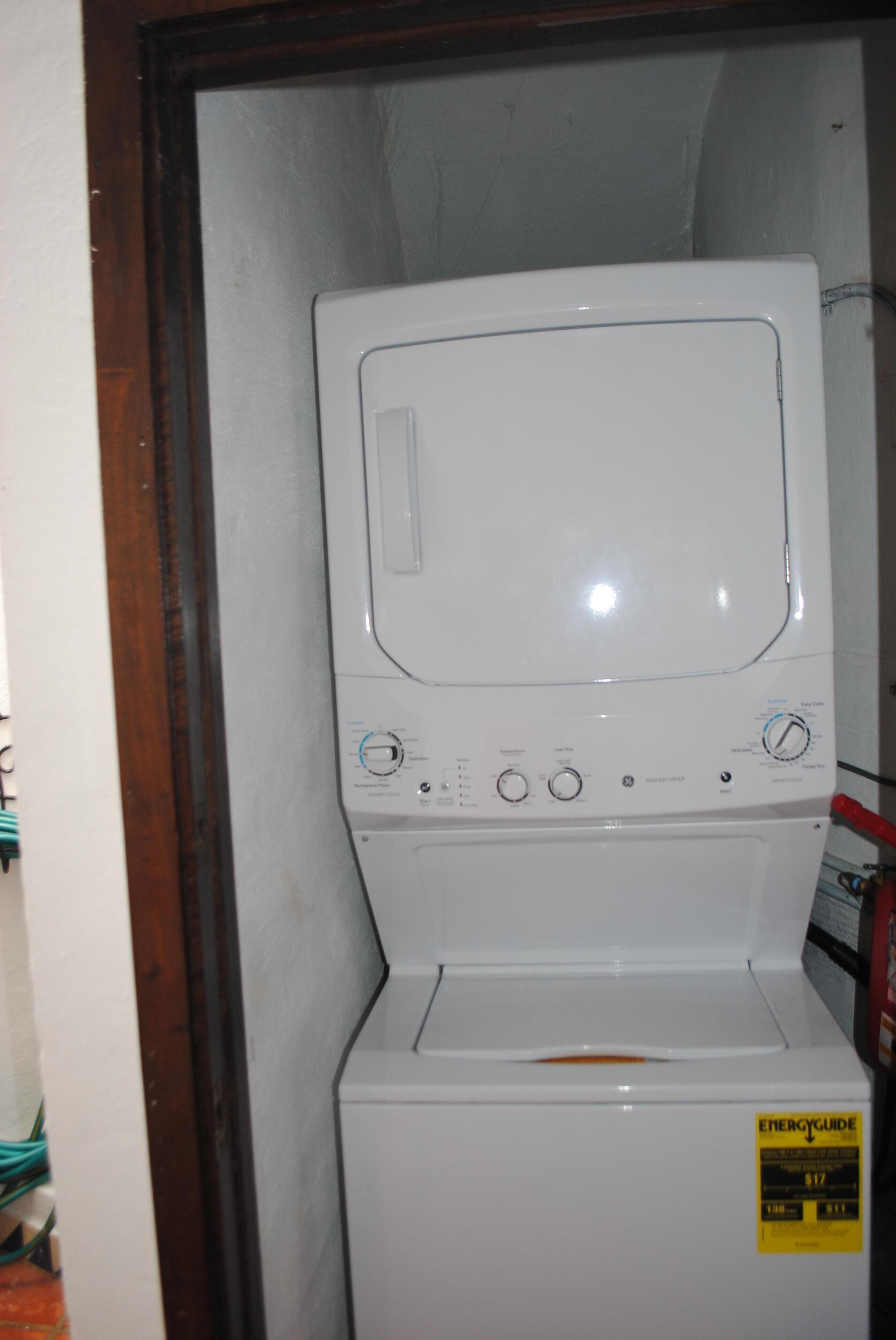 Una lavadora de carga frontal con un panel de control, una etiqueta amarilla de guía energética y un marco de puerta de madera.