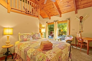 Un dormitorio con cama, una escalera de madera, un balcón con mesa y sillas, y vistas al exterior.
