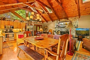 Un acogedor interior de cabaña con una mesa de comedor de madera, sillas, una chimenea, un televisor y una pared de piedra.