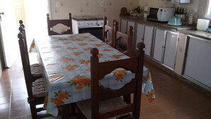 Ein Essbereich mit einem Tisch, der mit einer blumigen Tischdecke bedeckt ist, Holzstühle, einem Herd und einer Mikrowelle auf der Arbeitsfläche.