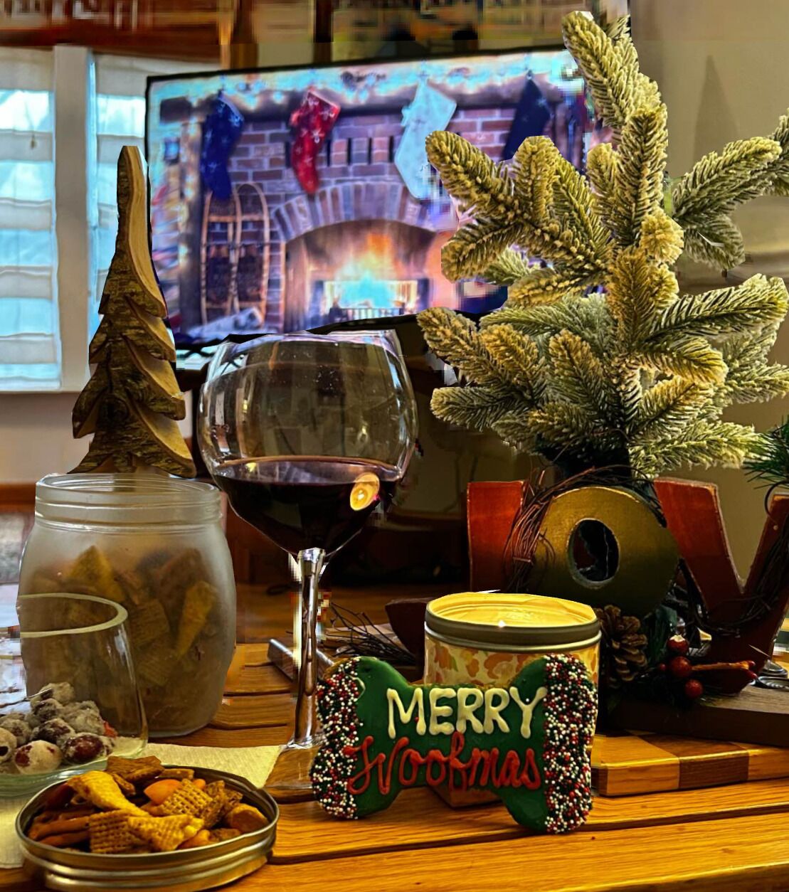 Una mesa festiva con una copa de vino tinto, un tarro de galletas, un pequeño árbol de Navidad y un cartel que dice 'Merry Christmas'.