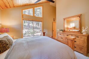 Relax in a serene bedroom with a large bed, wooden ceiling, and a forest view.