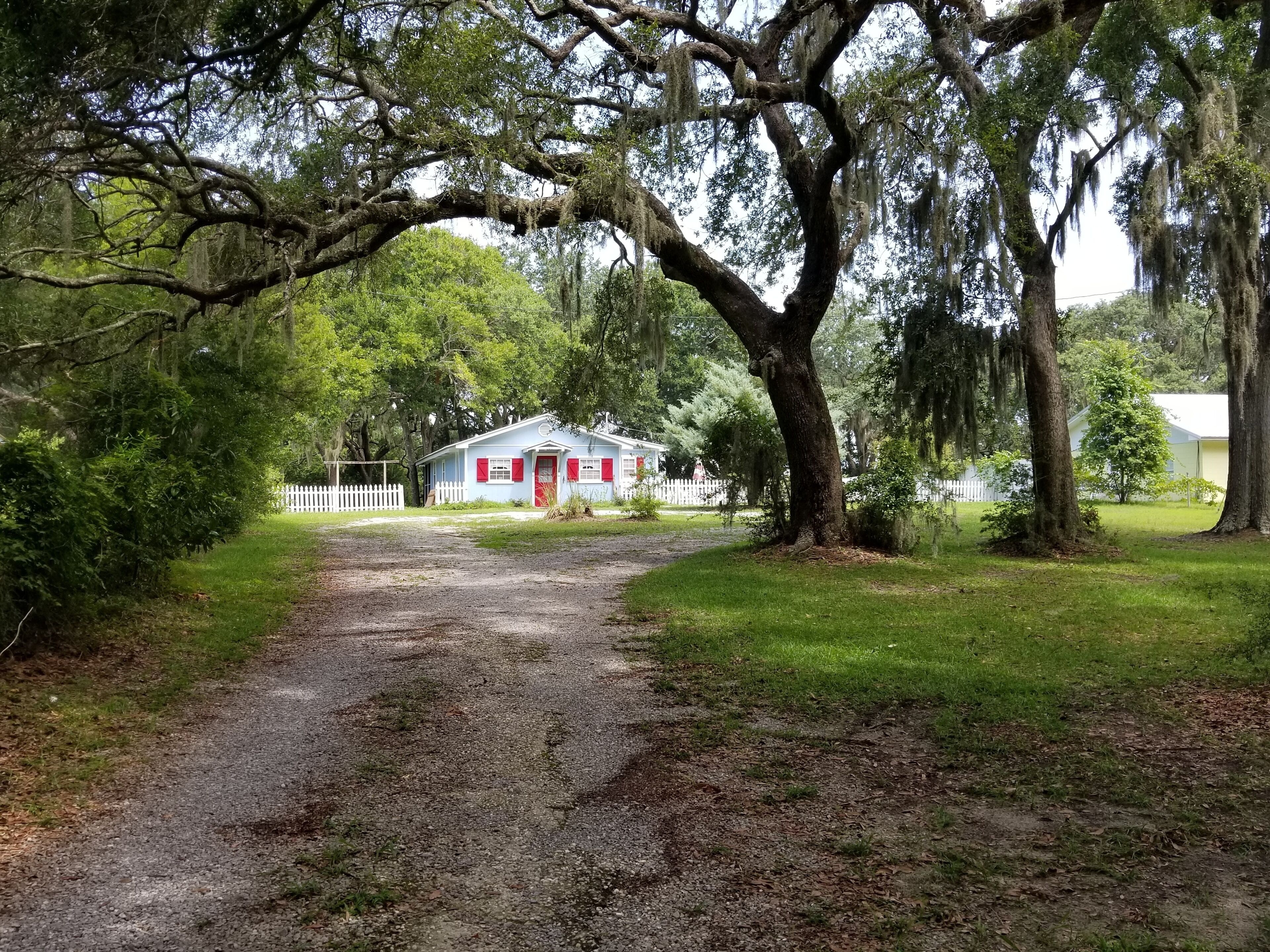 A rural property with a gravel driveway leading to a small house with a red door and white picket fence.
