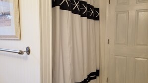 Een badkamer met een witte deur, een handdoekhouder en een douchegordijn met een zwart-wit patroon.