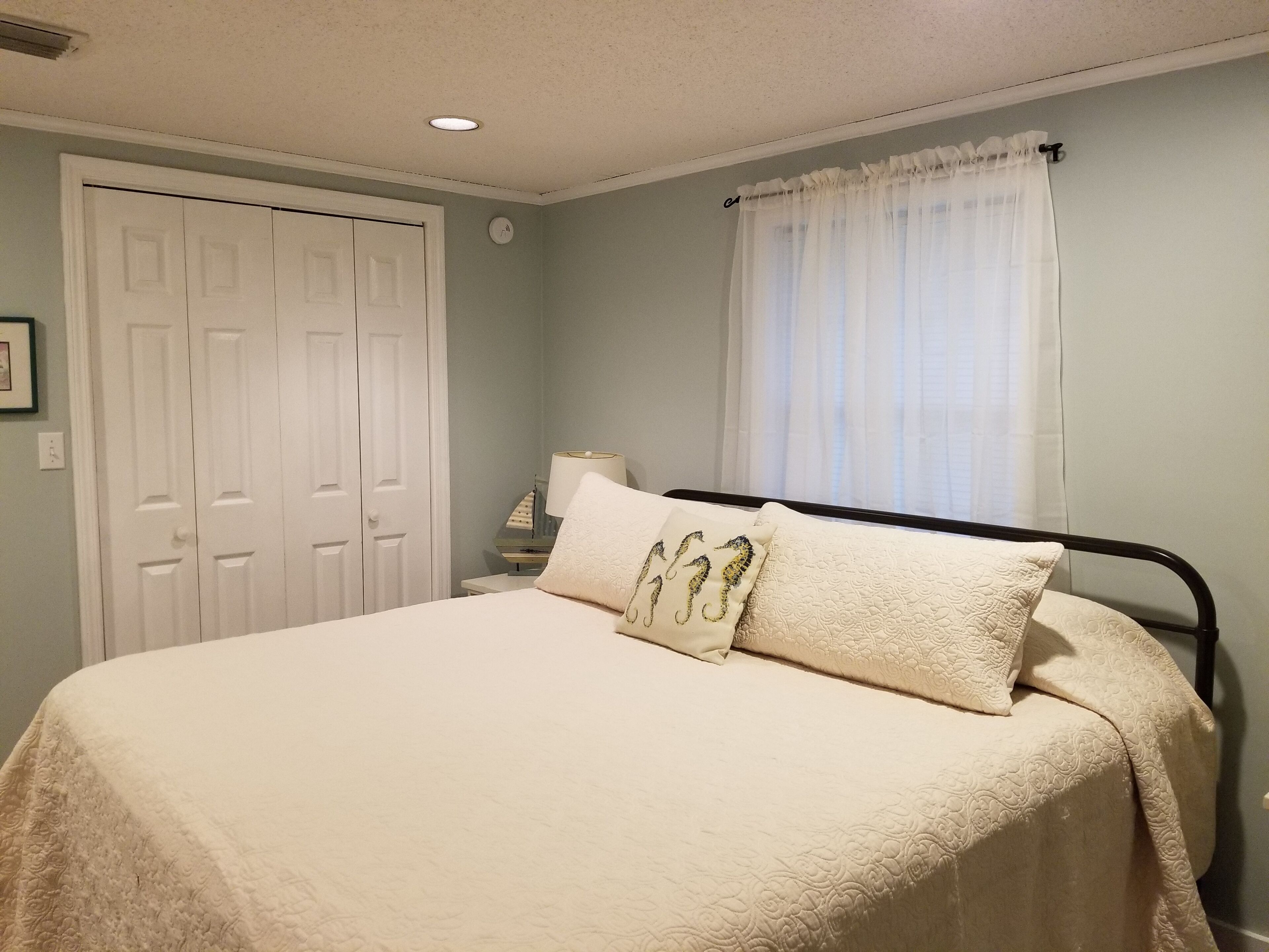 A bedroom with a bed, a nightstand, a lamp, a door, and a window with curtains.