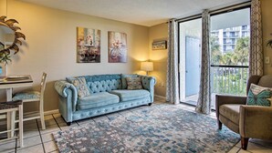 A living room with a sofa, a dining table, and chairs. There are paintings on the wall and a view of a balcony with a railing. - Gulf Shores Getaway w/ Pool, Spa & Beach Access! (Gulf Shores)