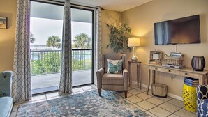 A living room with a sofa, armchair, and a TV on a wooden stand. A plant and a lamp are on a side table. - Gulf Shores Getaway w/ Pool, Spa & Beach Access! (Gulf Shores)