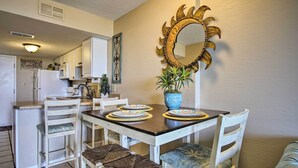 A dining area with a table set for four, white chairs, a decorative mirror, and a potted plant. - Gulf Shores Getaway w/ Pool, Spa & Beach Access! (Gulf Shores)