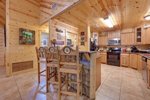 Un interior de madera con una cocina que incluye una isla de piedra, taburetes de bar de madera y un microondas.