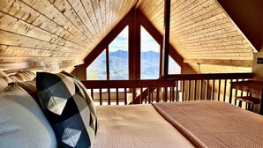 A cozy bedroom with a wooden ceiling, a large window, and a bed with pillows. - Mountain Time | Scenic Views, Hot Tub, Wi-Fi, & Shuffleboard (Bryson City)