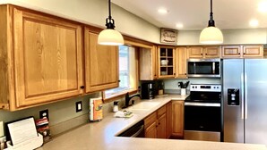 A kitchen with wooden cabinets, a stainless steel refrigerator, a microwave, and a coffee maker. - Mountain Time | Scenic Views, Hot Tub, Wi-Fi, & Shuffleboard (Bryson City)