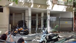 Une entrée fermée par un portail, avec un espace de stationnement couvert, une moto et un scooter garés devant.