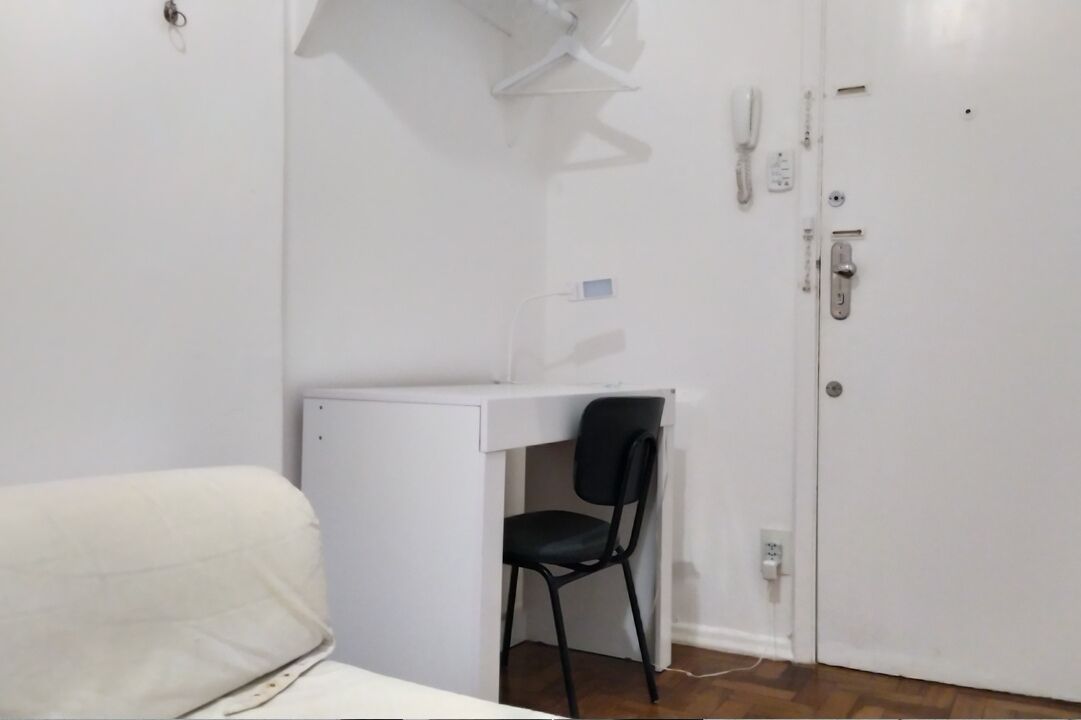 Una habitación pequeña y blanca con un escritorio, una silla negra y un sofá blanco.