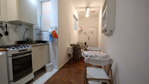Une cuisine compacte équipée d’une cuisinière à gaz, d’un four et de meubles blancs. On y trouve également un petit coin repas avec une table et des chaises.