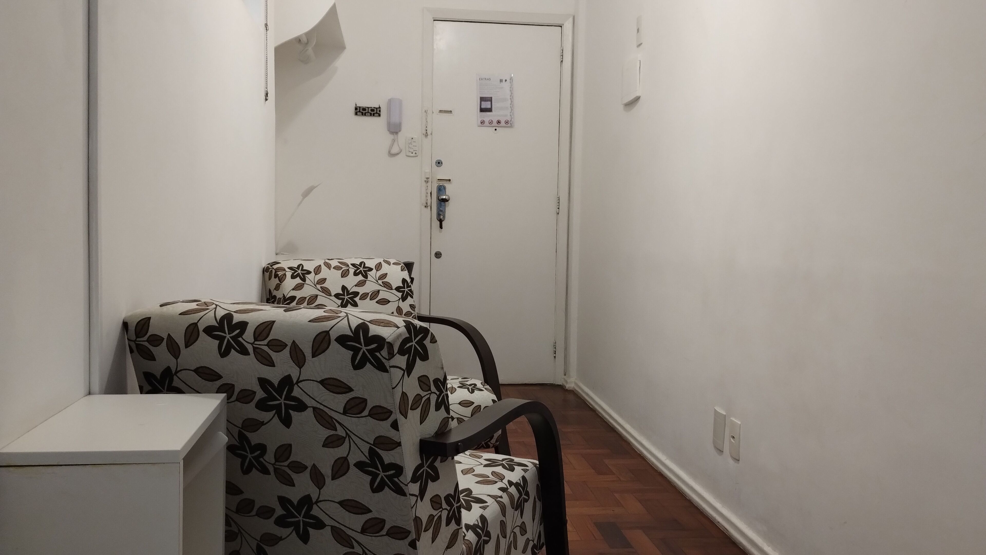 Ein schmales Entree mit einem blumengemusterten Sessel und einem weißen Schrank.
